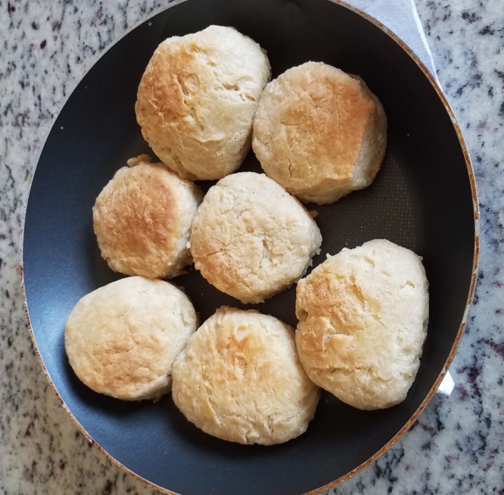 Eight golden-brown biscuits from a home test batch, brought inside in a frying pan