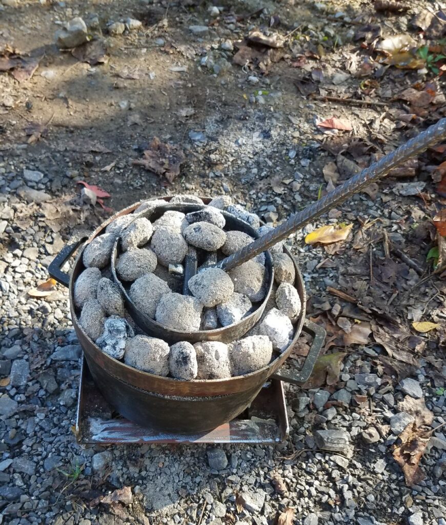 Dutch oven baking on its stand, with charcoal briquettes held in rings on the lid