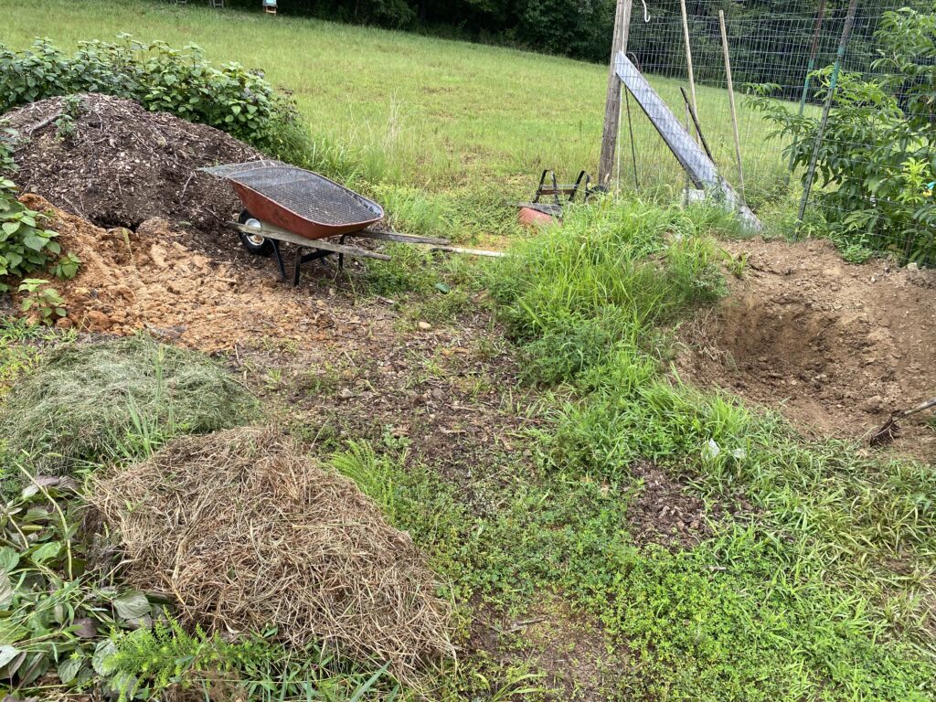 Garden area with piles of hay, grass clippings, wood chips and dirt next to a wheelbarrow