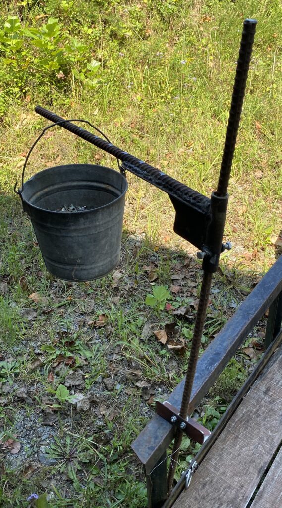 Prototype of a steel cooking stand: a rebar post with a swing arm holding a bucket of nails as a test weight