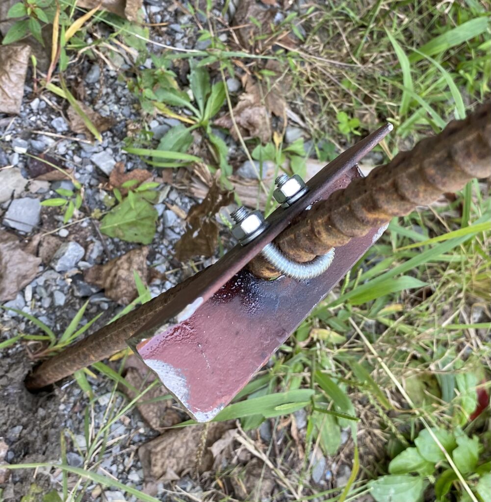 Steel bracket bolted to the rebar post, resting on the fire ring edge to stop the post swaying
